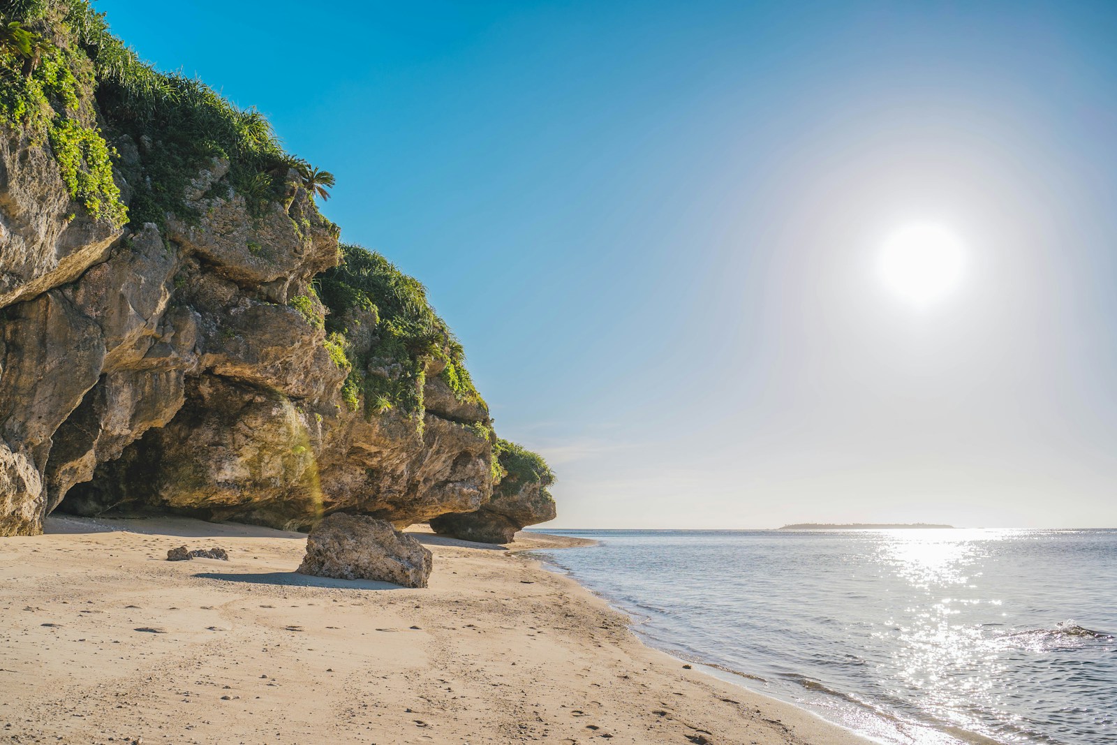 the sun is shining over a rocky cliff on the beach